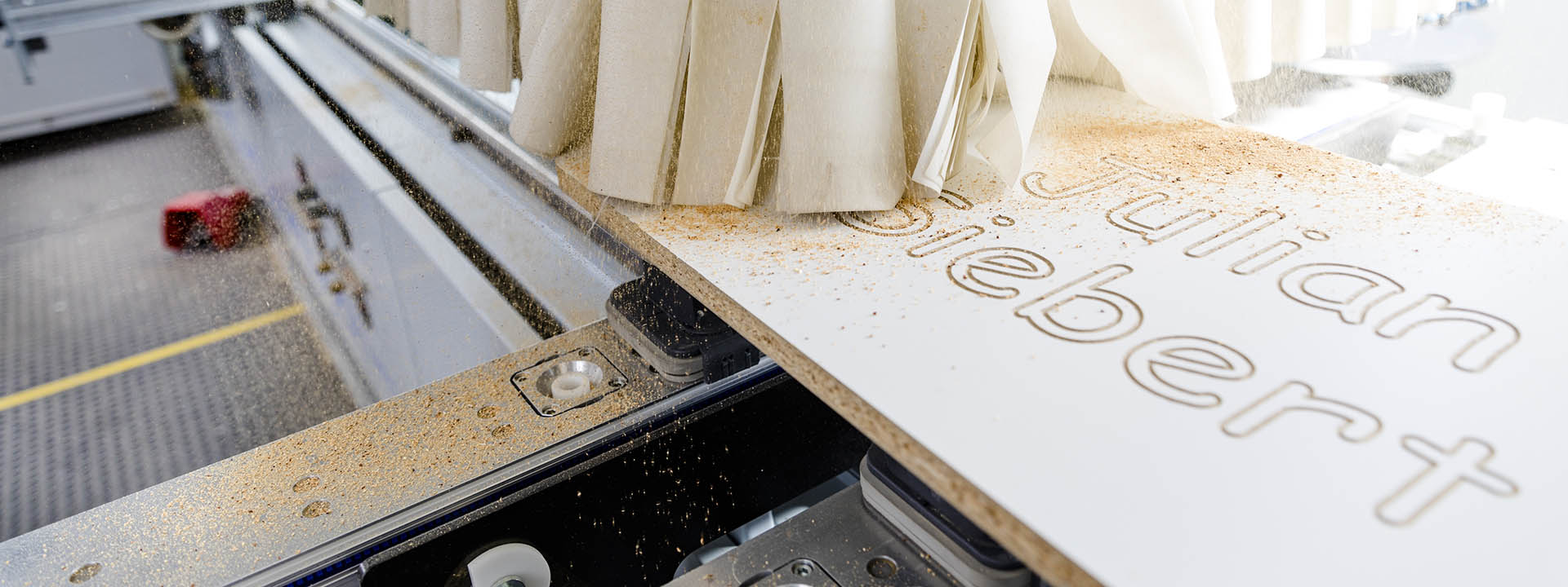 Nahaufnahme einer CNC-Maschine beim Fr&auml;sen einer Holzplatte mit Holzsp&auml;nen in der Werkstatt