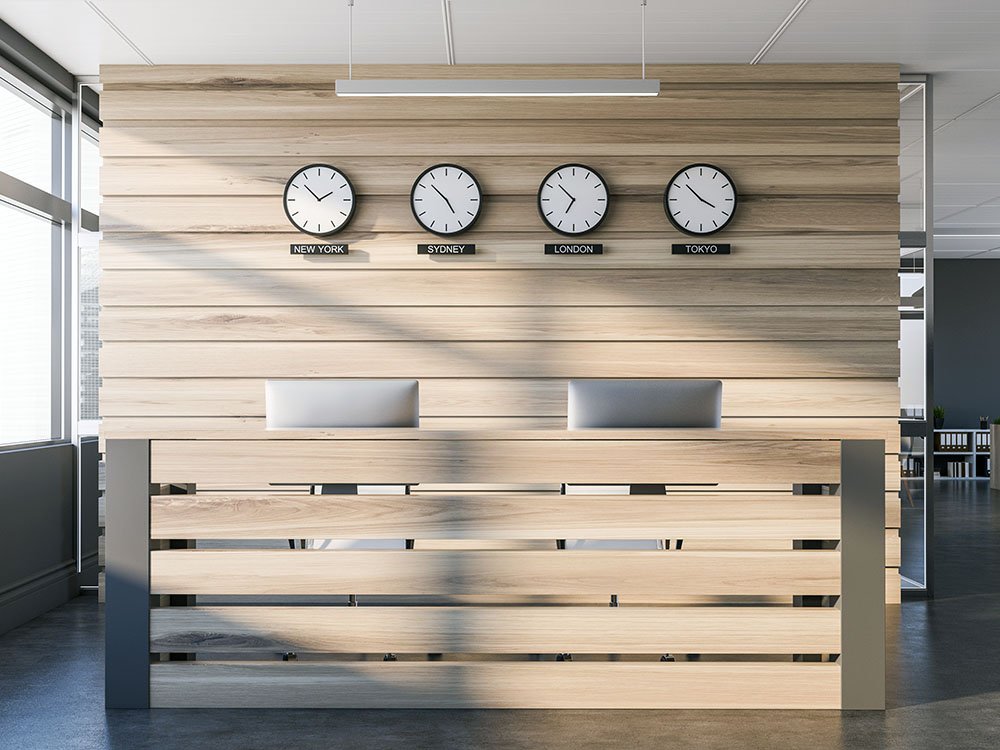 Moderner Empfangstresen aus hellem Holz mit integrierten Uhren – Beispiel für individuellen Objektbau