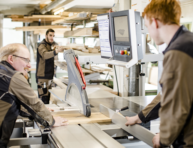 Mehrere Tischler arbeiten gemeinsam an einer Formatkreissäge – präzise Holzbearbeitung in der Werkstatt